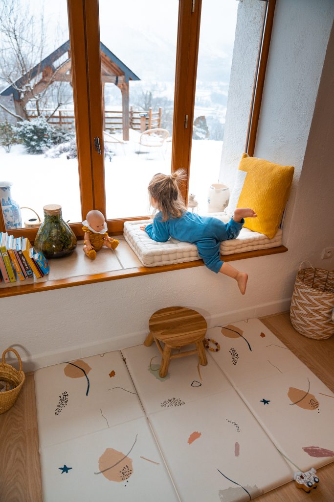 bébé regarde par la fenêtre en hiver sous la neige